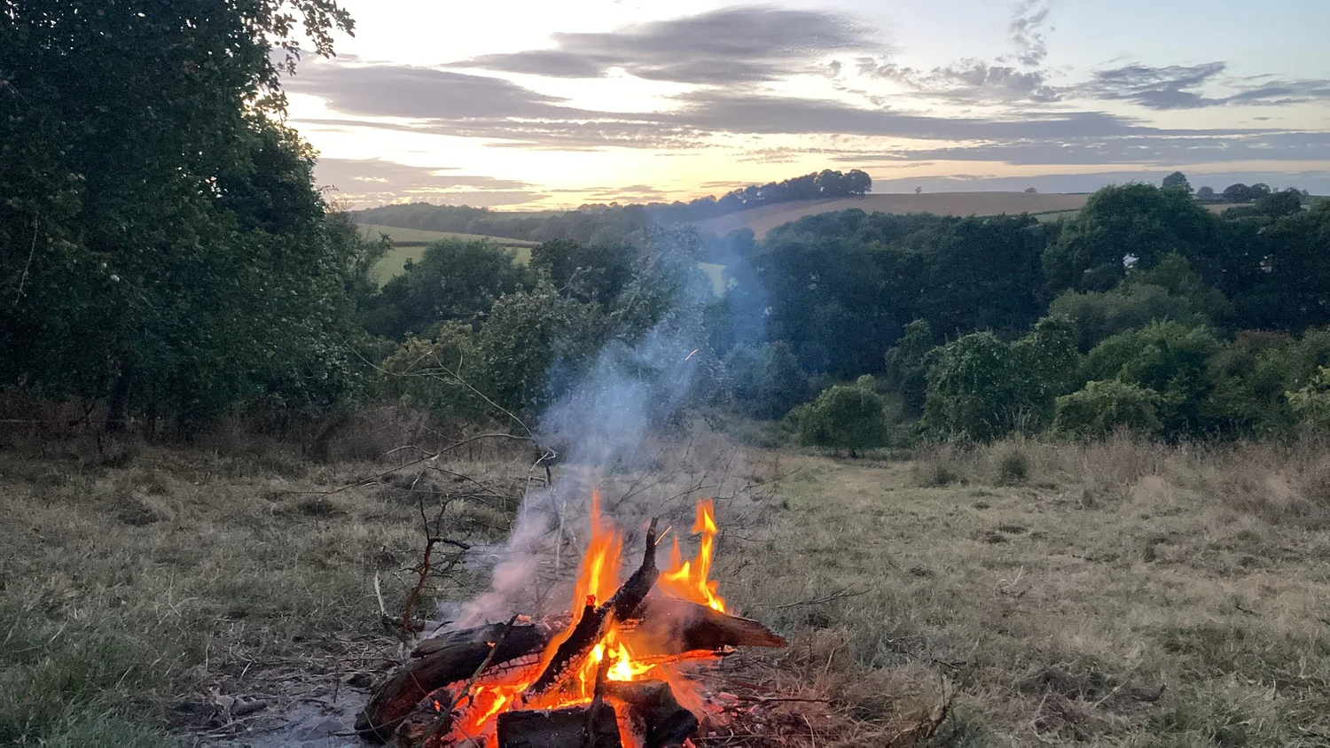 A bonfire burning at dusk with rolling Devon hills behind